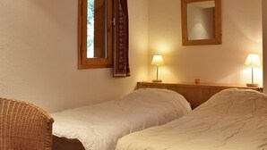 Ein Schlafzimmer mit zwei Einzelbetten, einem Holz-Kopfteil, einem Fenster mit Vorhängen, einem Spiegel und zwei Nachttischlampen.