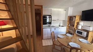 Eine kompakte Küche mit weißen Schränken, einem Geschirrspüler, einer Mikrowelle und einem Essbereich mit Holztisch und Stühlen.