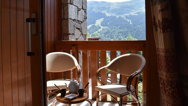 Ein Balkon mit Korbstühlen, einem kleinen Tisch mit Teekanne und Tassen sowie einer Steinmauer.