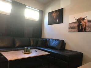 A modern living room with a black leather sofa, a wooden coffee table with candles, and two framed pictures on the wall. - Notodden Sentrum Apartment NO 10 (Notodden)
