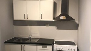 A compact kitchen with white cabinets, a black countertop, a stainless steel sink, and a white stove. - Notodden Sentrum Apartment NO 10 (Notodden)