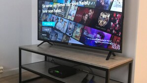 A flat-screen TV on a black metal TV stand with a Netflix interface displaying various shows and movies. - Notodden Sentrum Apartment NO 10 (Notodden)