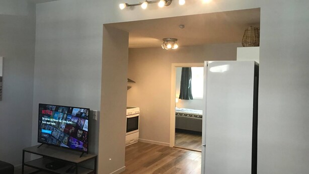 A compact living space with a television on a stand, a refrigerator, and a wooden floor. - Notodden Sentrum Apartment NO 10 (Notodden)