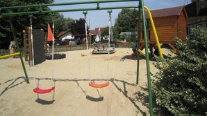 Een speeltuin met schommels en een glijbaan, omringd door zand en groen.