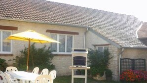 A patio with a table and chairs, a yellow umbrella, and a stone building with a tiled roof.