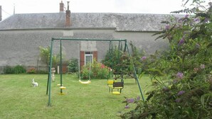 A grassy yard with a swing set, a dog, and a building in the background.
