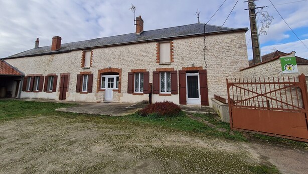A two-story stone building with a gated entrance, a small front porch, and a sign indicating it is a Gîte.