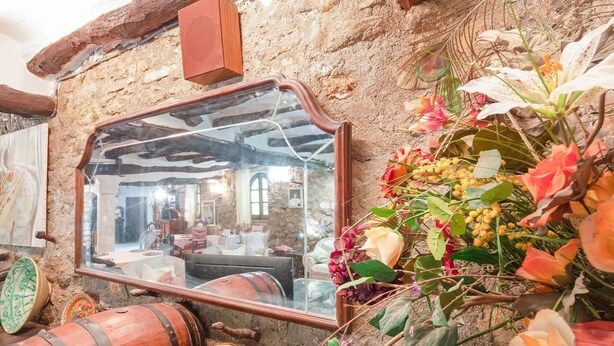 A rustic interior with a stone wall, wooden barrels, and a mirror reflecting a cozy room.