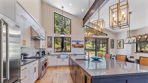 A modern kitchen with a large island, stainless steel appliances, and large windows offering views of the outdoors.