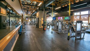 A spacious gym with various exercise equipment, wooden beams on the ceiling, and large windows allowing natural light.