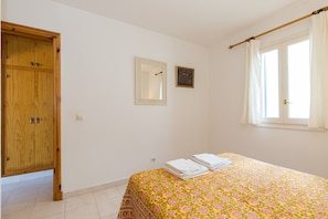 Une chambre à coucher avec un lit, une armoire en bois, un miroir et une fenêtre avec des rideaux.