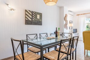 Un comedor con mesa de vidrio, sillas tejidas, un cuadro en la pared, una lámpara y un televisor.