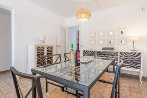 A dining area with a glass table, chairs, a zebra-patterned cabinet, and a hanging light fixture.