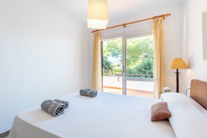 A hotel room with a bed, a window with curtains, a lamp, and a view of greenery outside.