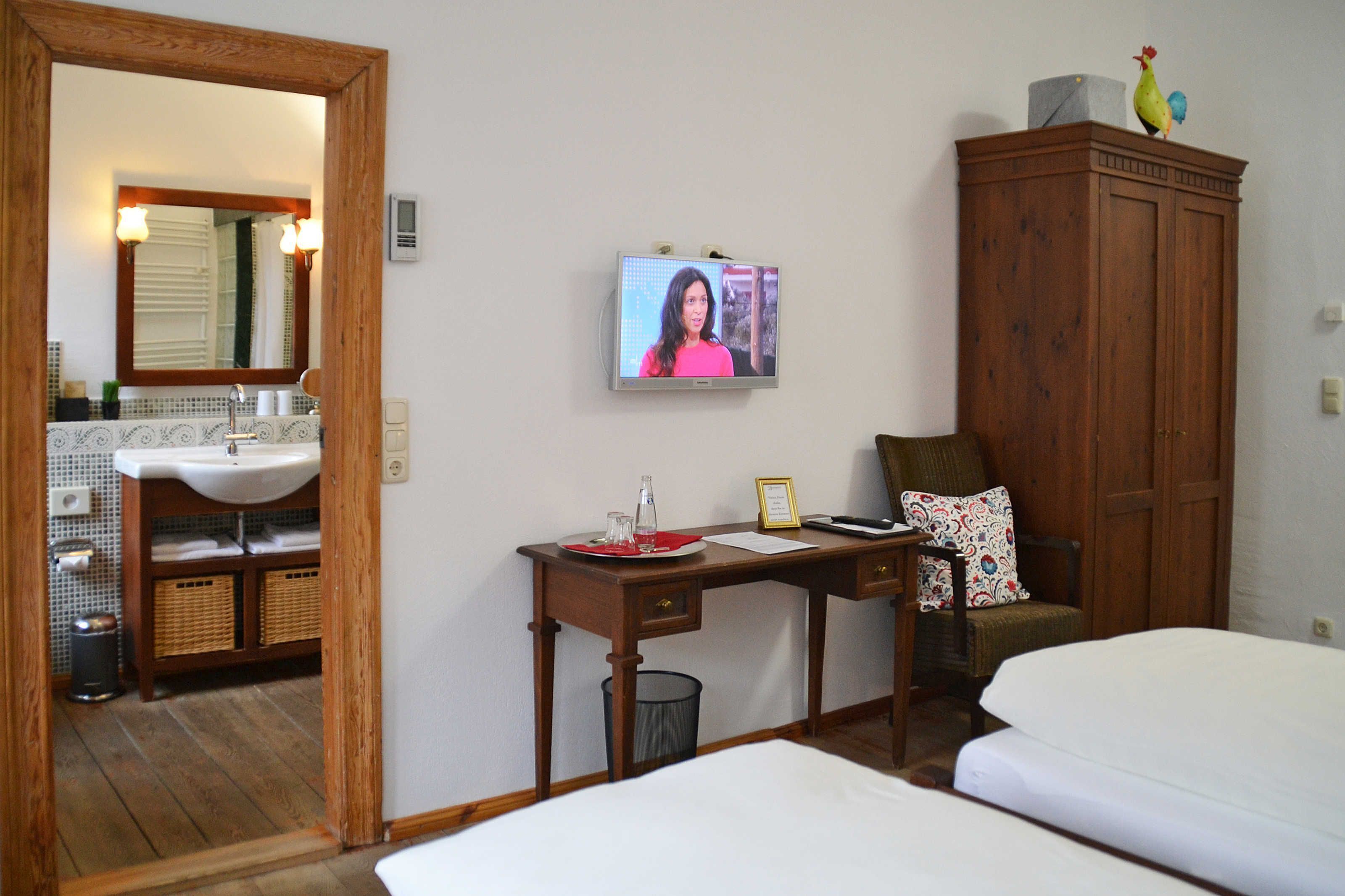 Ein Hotelzimmer mit einem Holztisch, einem Sessel, einem Bett, einem Fernseher und einem Kleiderschrank.