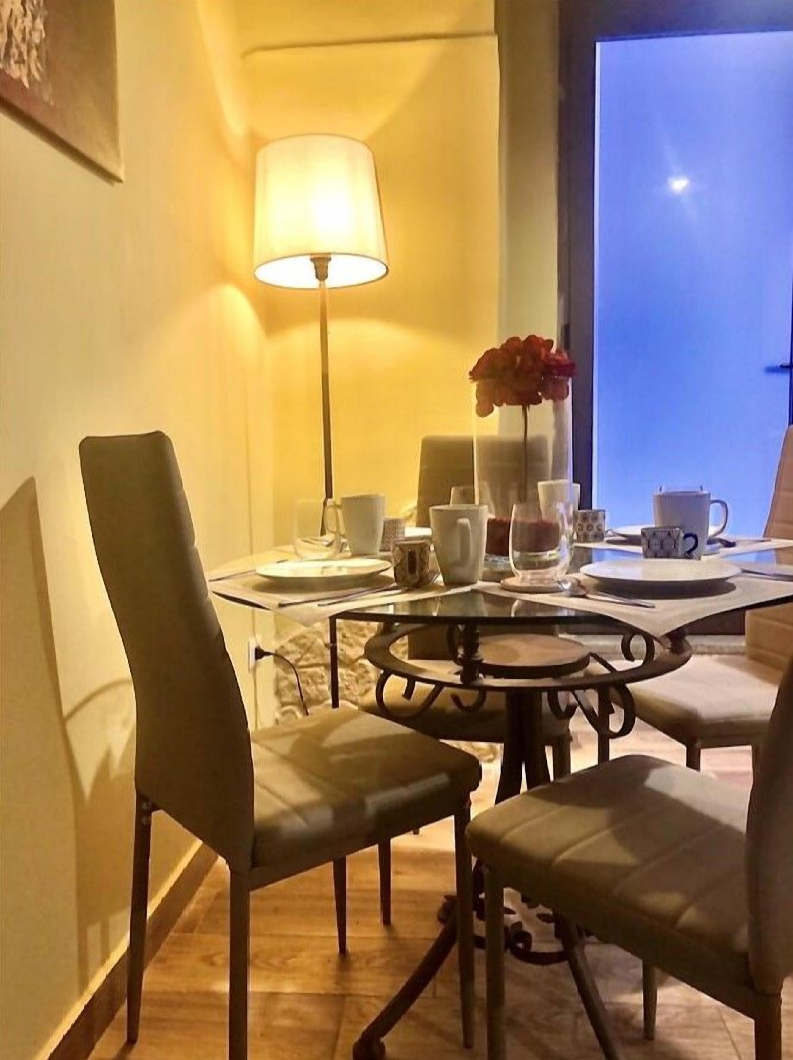 A dining area with a table set for two, a lamp, and a vase with flowers.