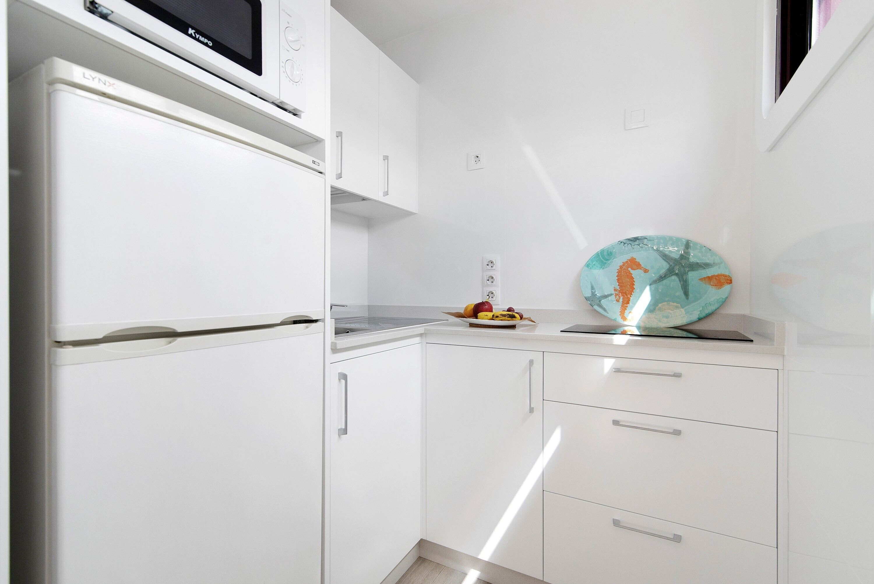 Una cocina compacta con muebles blancos, un microondas y un frutero sobre la encimera.