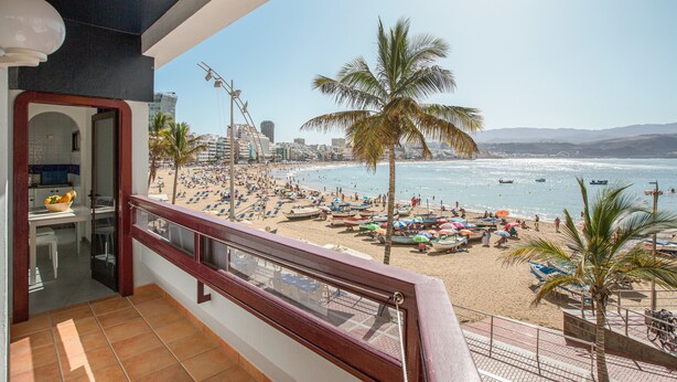 Ein Balkon mit Blick auf einen Strand, Palmen und eine Stadtlandschaft im Hintergrund.