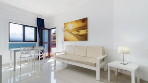 Ein modernes Wohnzimmer mit einer Couch, einem Esstisch mit Stühlen, einer Lampe und einem großen Fenster mit Aussicht.