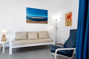 A room with a white sofa, a blue armchair, a floor lamp, and a painting of a landscape.