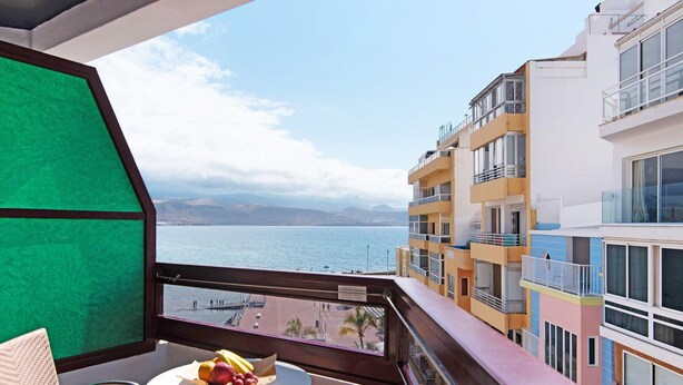 Un balcon avec une table, une chaise et une vue sur la mer et les bâtiments.