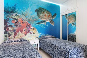 Une chambre avec deux lits, une table de chevet et une fresque représentant une tortue sur le mur.