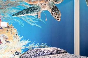 Une chambre ornée d’une fresque représentant une tortue de mer, avec un lit recouvert d’une literie à motifs et un mur bleu.