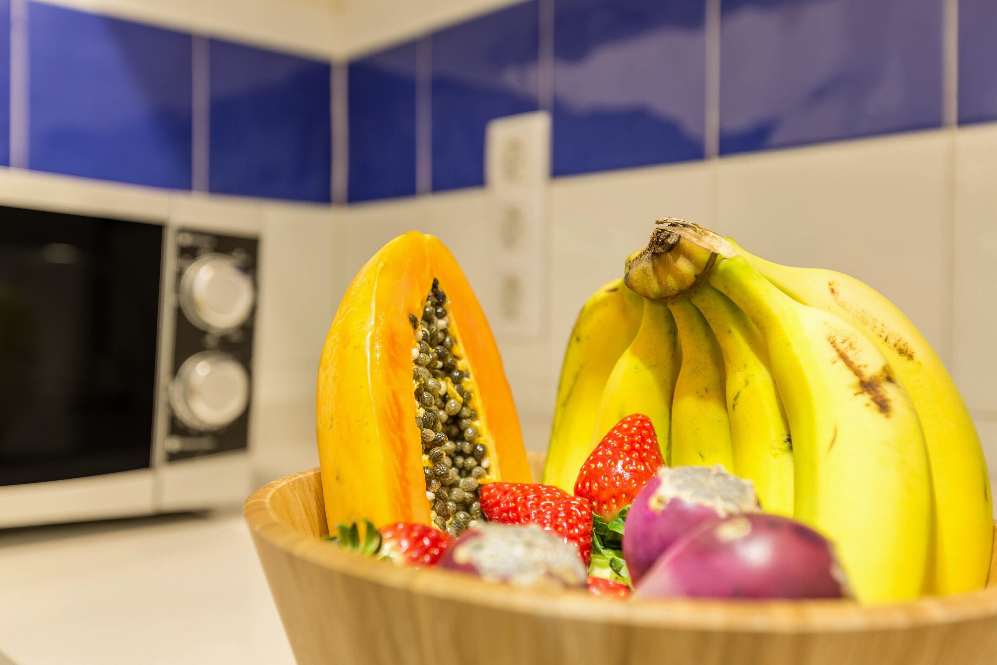 A bowl of fruit in a kitchen with a microwave and blue cabinets.