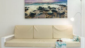 A white sofa with beige cushions, a framed beach scene, and a floor lamp. - Vacation Rental “Studio 50” with Sea View, Terrace & Wi-Fi (Las Palmas de Gran Canari)