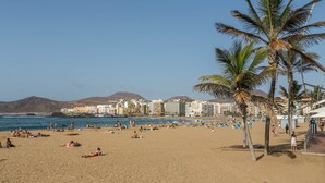 A beach with palm trees, people sunbathing, and buildings in the background. - Vacation Rental “Studio 50” with Sea View, Terrace & Wi-Fi (Las Palmas de Gran Canari)