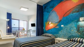 A hotel room with a bed, a desk, a chair, a TV, and a large fish mural on the wall. - Vacation Rental “Studio 50” with Sea View, Terrace & Wi-Fi (Las Palmas de Gran Canari)