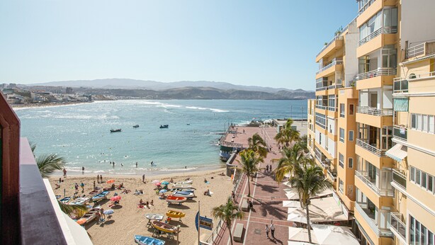Un hotel sulla costa con balconi, spiaggia e barche.