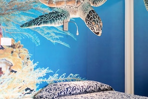 Een kamer met een muurschildering van een zeeschildpad, een bed met decoratieve beddengoed en een blauwe wand.
