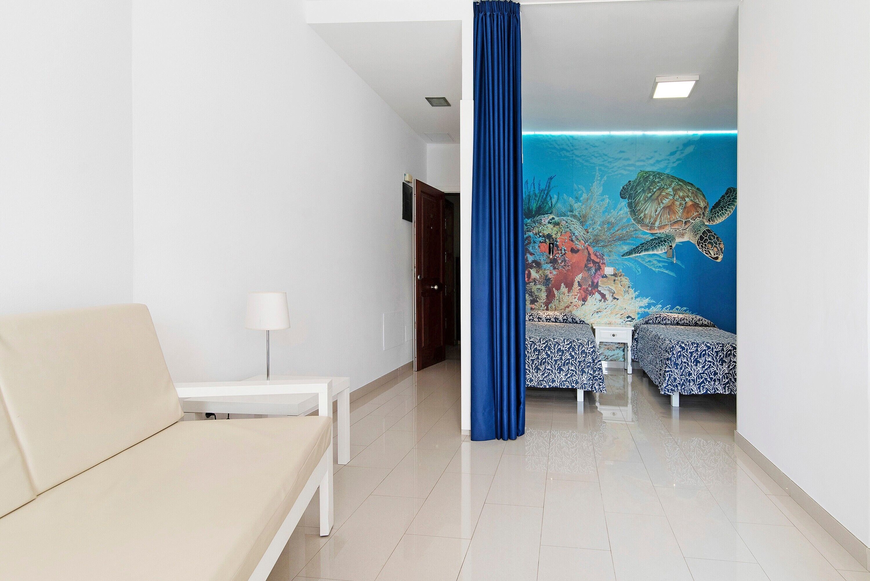 A hotel room with a bed, a sofa, a small table, and a mural of a turtle on the wall.
