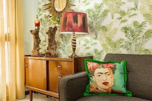 A room with a wooden cabinet, a lamp, a sofa with a pillow, and a wall with a leaf pattern.