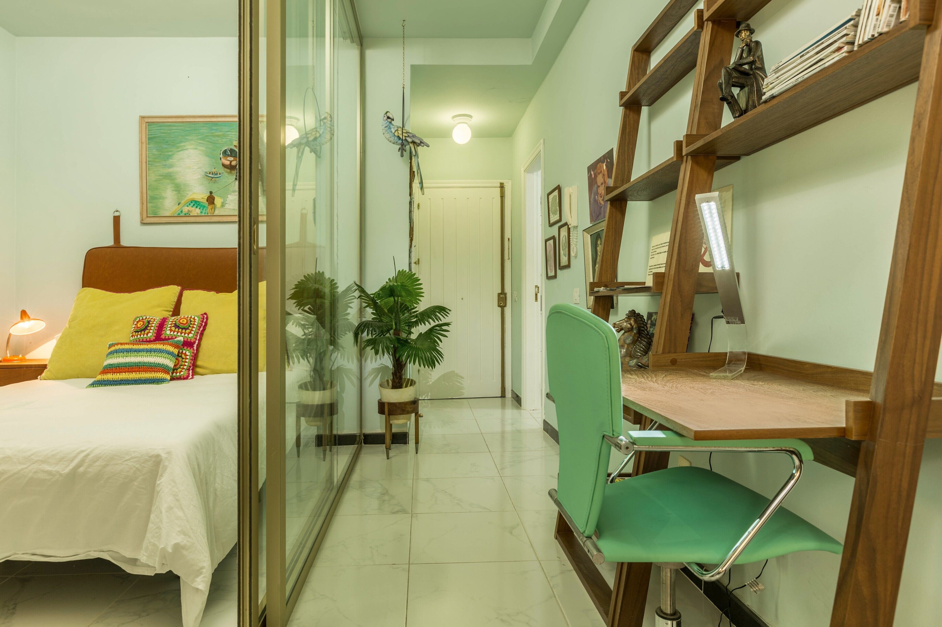 Un dormitorio con cama, mesita de noche, lámpara y una silla verde.