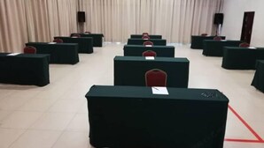 A conference room with rows of tables and chairs, a stage with a podium, and curtains on the walls.