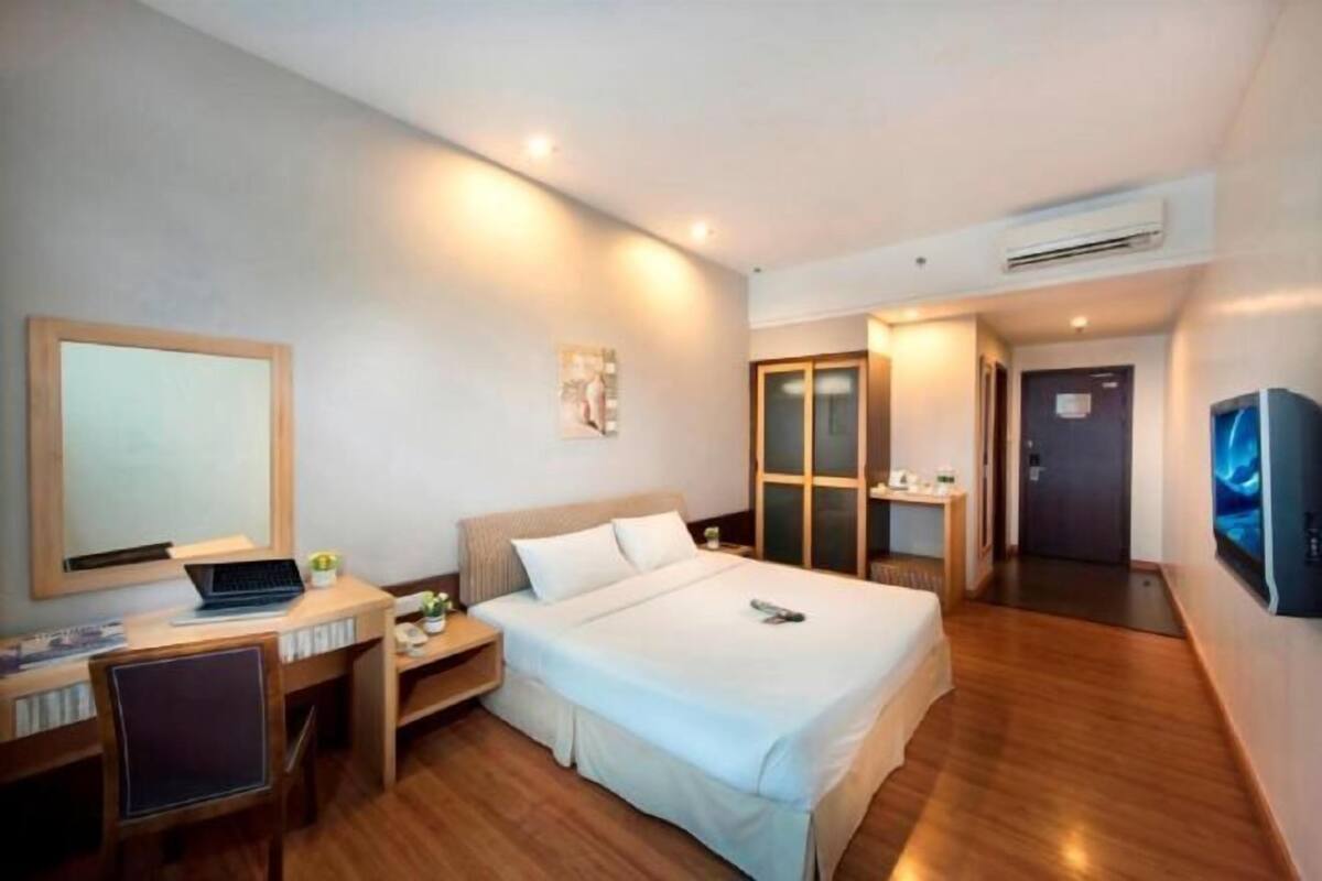 Een hotelkamer met een bed, een bureau met een laptop, een televisie en een airconditioner.