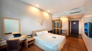 A hotel room with a bed, a desk with a laptop, a TV, and an air conditioning unit.