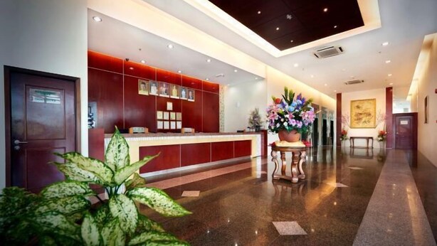A modern hotel lobby with a reception desk, a large potted plant, and a painting on the wall.