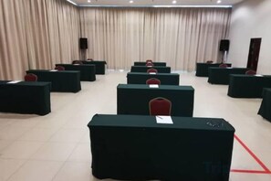 Een congrescentrum met rijen tafels en stoelen, een podium met lessenaar, en gordijnen aan de muren.