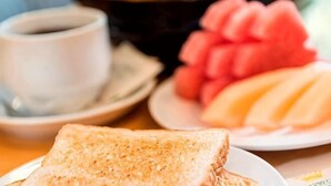 Une table mise pour le petit-déjeuner avec une assiette de toasts, un bol de fruits et une tasse de café.