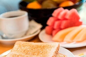 Un desayuno con tostadas, un tazón de fruta y una taza de café.
