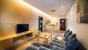 A modern living room with a flat-screen TV, a sofa, a coffee table, and a kitchen in the background.