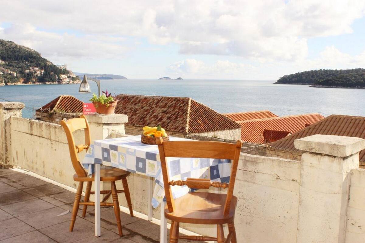 A terrace with a table and chairs overlooking a coastal view.