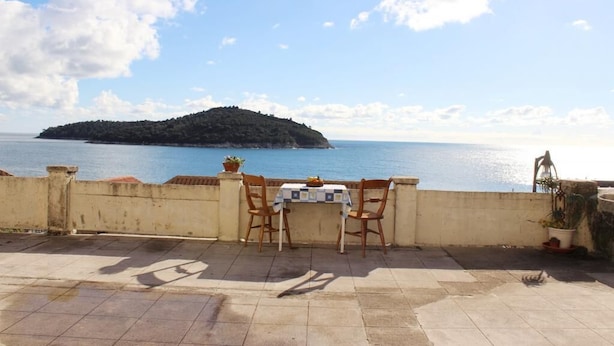 A terrace with a table and chairs overlooking a body of water and a small island. - Room Lazareti (Dubrovnik)