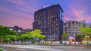 A multi-story hotel with illuminated signage, surrounded by trees and other buildings. - Lavande Hotel (Jiangmen)