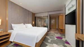 A hotel room with a large bed, a TV, a bathroom with a glass door, and a patterned carpet. - Lavande Hotel (Jiangmen)