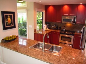 A kitchen with granite countertops, stainless steel appliances, and red cabinetry. - Kapalua Ridge Villa 1214 Gold Ocean View (Lahaina)