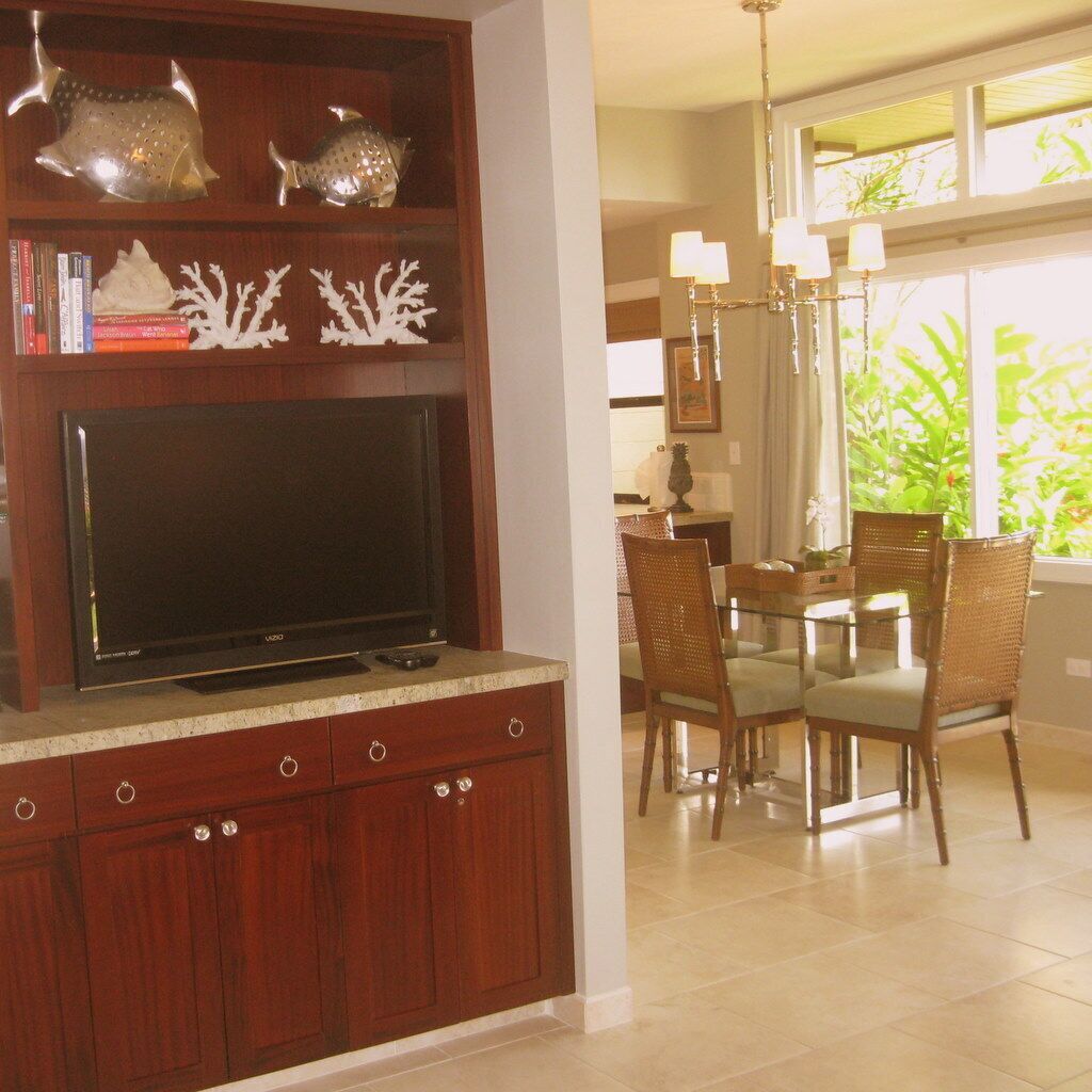A modern kitchen with a flat-screen TV, wooden cabinets, and a dining area with wicker chairs and a glass table.
